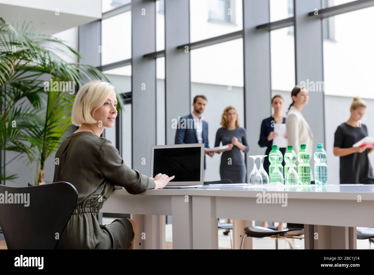 Geschäftsfrau, die in Bürogebäude arbeitet, während Kollegen auf ein Geschäftstreffen anstehen Stockfoto