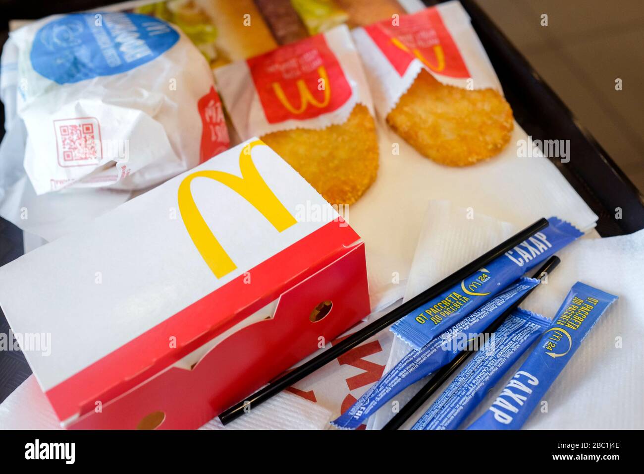 Essen bei McDonald's. Eine Reihe von Frühstücksprodukten auf einem Tablett Dranik, einrosafarbene Zuckerpakete, Burger, Servietten, Strohhalme. Stockfoto