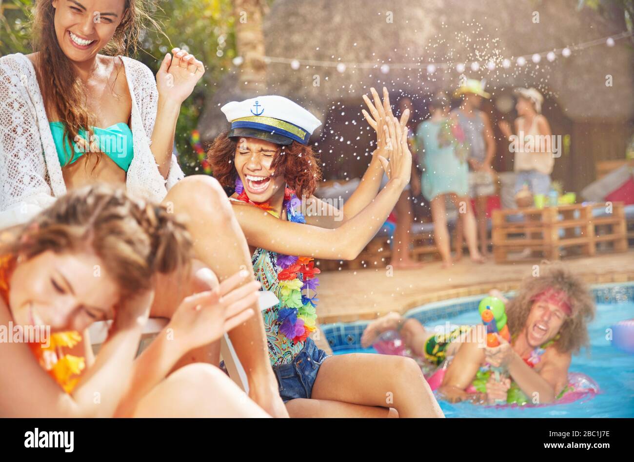 Junger Mann mit Hauspistole sprüht Frauen Freunde im Sommer-Schwimmbad Stockfoto