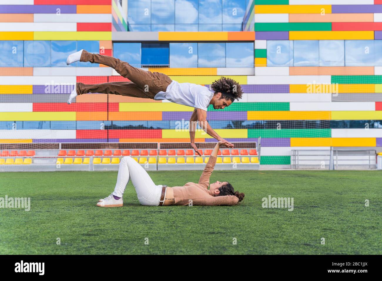 Tänzerin springt in der Luft über den Partner, auf Gras liegend Stockfoto