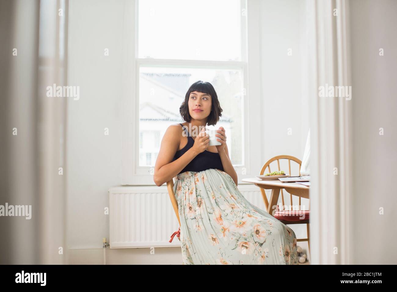 Nachdenkliche schwangere Frau trinkt Tee in der Wohnung Stockfoto