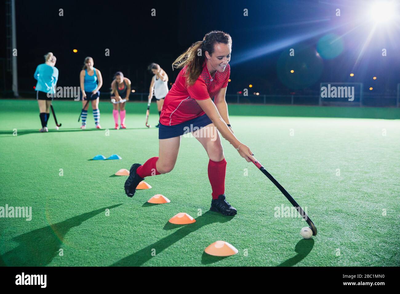 Entschlossener junger Feldhockeyspieler, der nachts Sportübung auf dem Feld ausübt Stockfoto