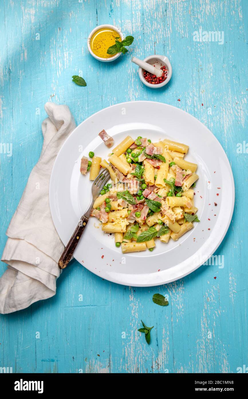 Italienisches Rezept Pasta tortilloni mit grünem Erbsen, Minzblättern, Vlies, geräuchertem Speck und Käse. Draufsicht, blauer Hintergrund. Stockfoto