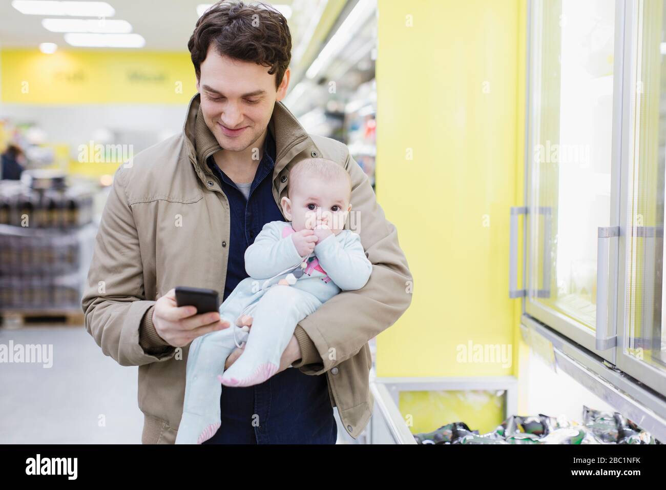 Vater mit Tochter überprüft Smartphone, kauft im Supermarkt ein Stockfoto
