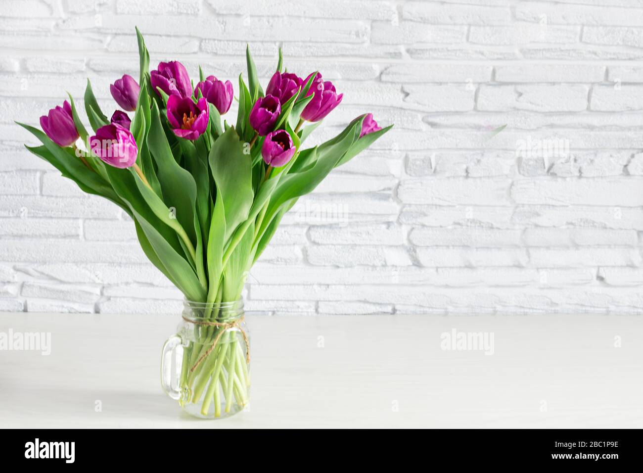 Wunderschöner Blumenstrauß aus violettem Tulpenblumen auf weißem Regal vor weißer Ziegelwand. Kopierbereich. Stockfoto