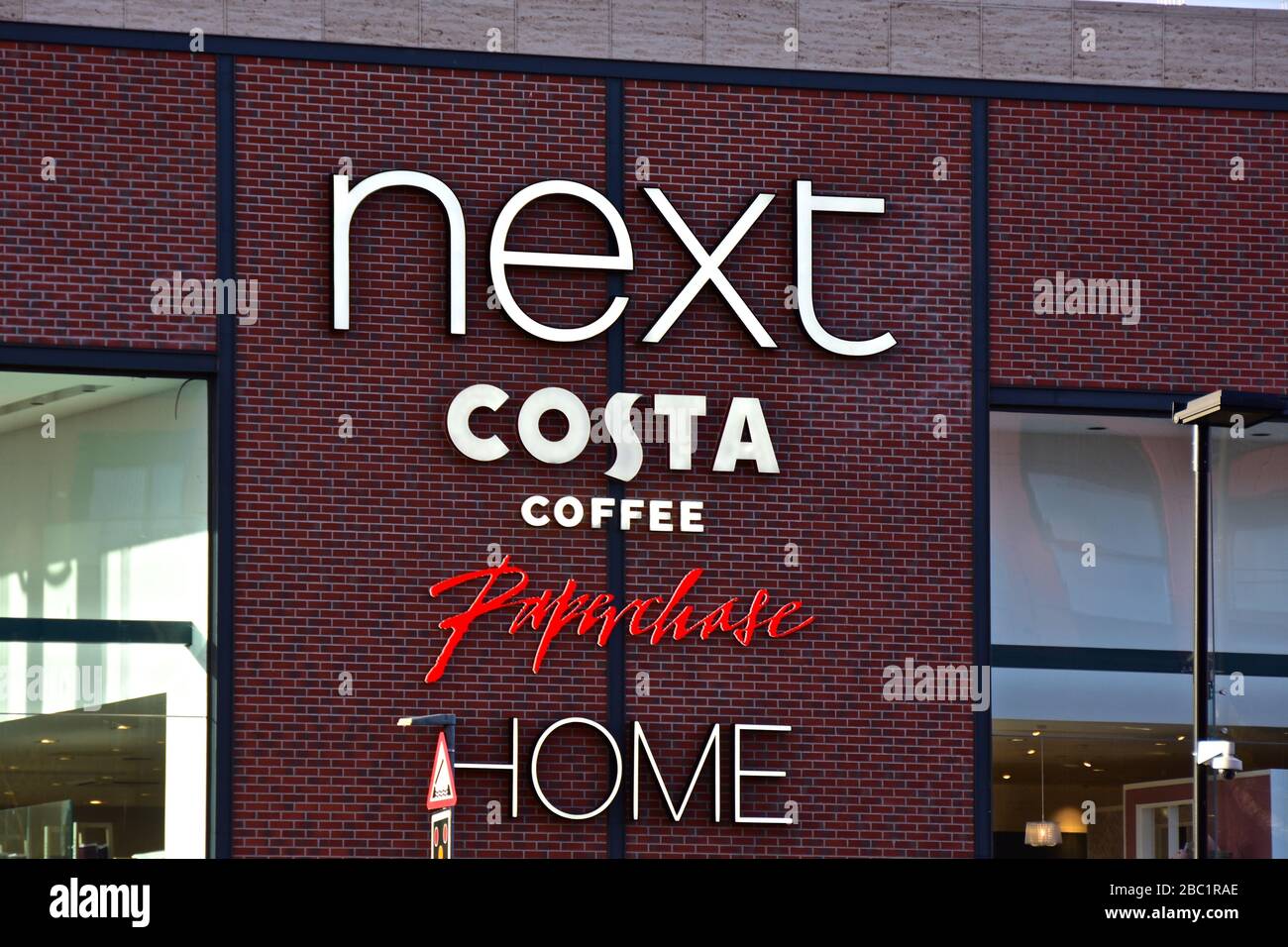 Das Schild an der Wand des modernen Next Retail Modeshops mit Inneneinrichtung und einem Costa Coffee Shop. Stockfoto