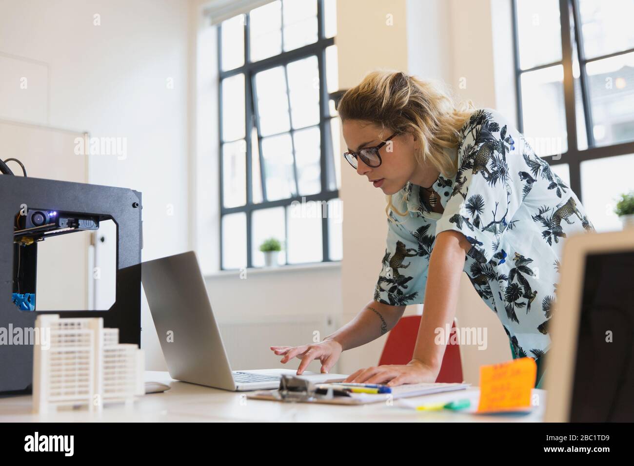 Designerin arbeitet am Laptop neben dem 3D-Drucker im Büro Stockfoto