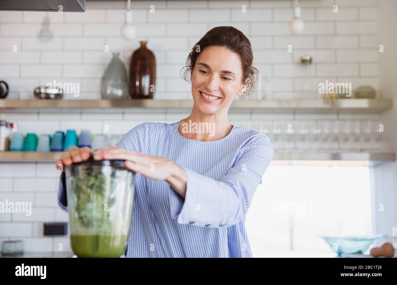 Lächelnde Frau, die in der Küche gesunden grünen Smoothie im Mixer zubereitet Stockfoto