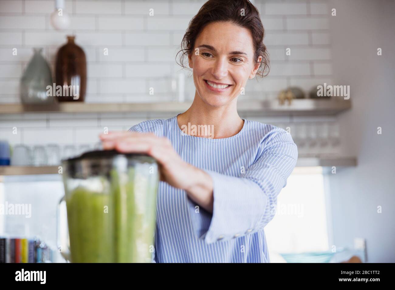 Lächelnde Frau, die in der Küche einen gesunden grünen Smoothie macht Stockfoto