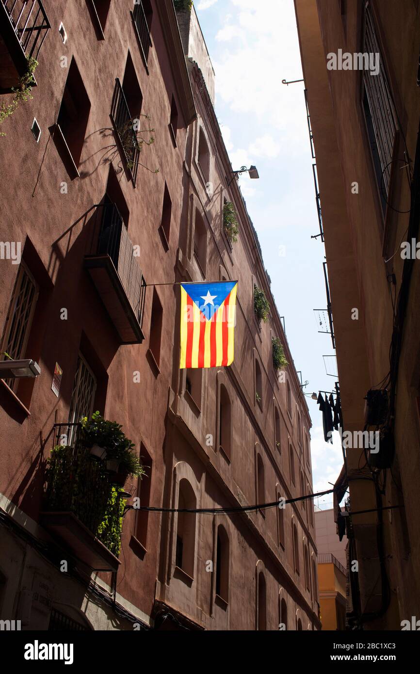 Blick auf die katalanische Flagge, die an der schmalen Straße und an historischen, alten Gebäuden im Viertel "Ciutat Vella" (gotisches Viertel) in Barcelona hing. Es ist eine sonnige Summe Stockfoto