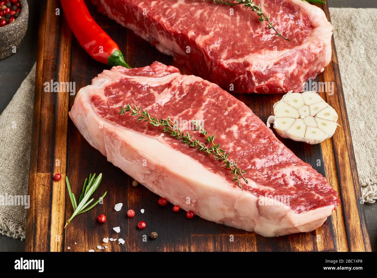 Würzen von rohem Steak mit Salz, Thymian, Knoblauch. Zwei große ganze Stück rohes Rindfleisch Fleisch Stockfoto