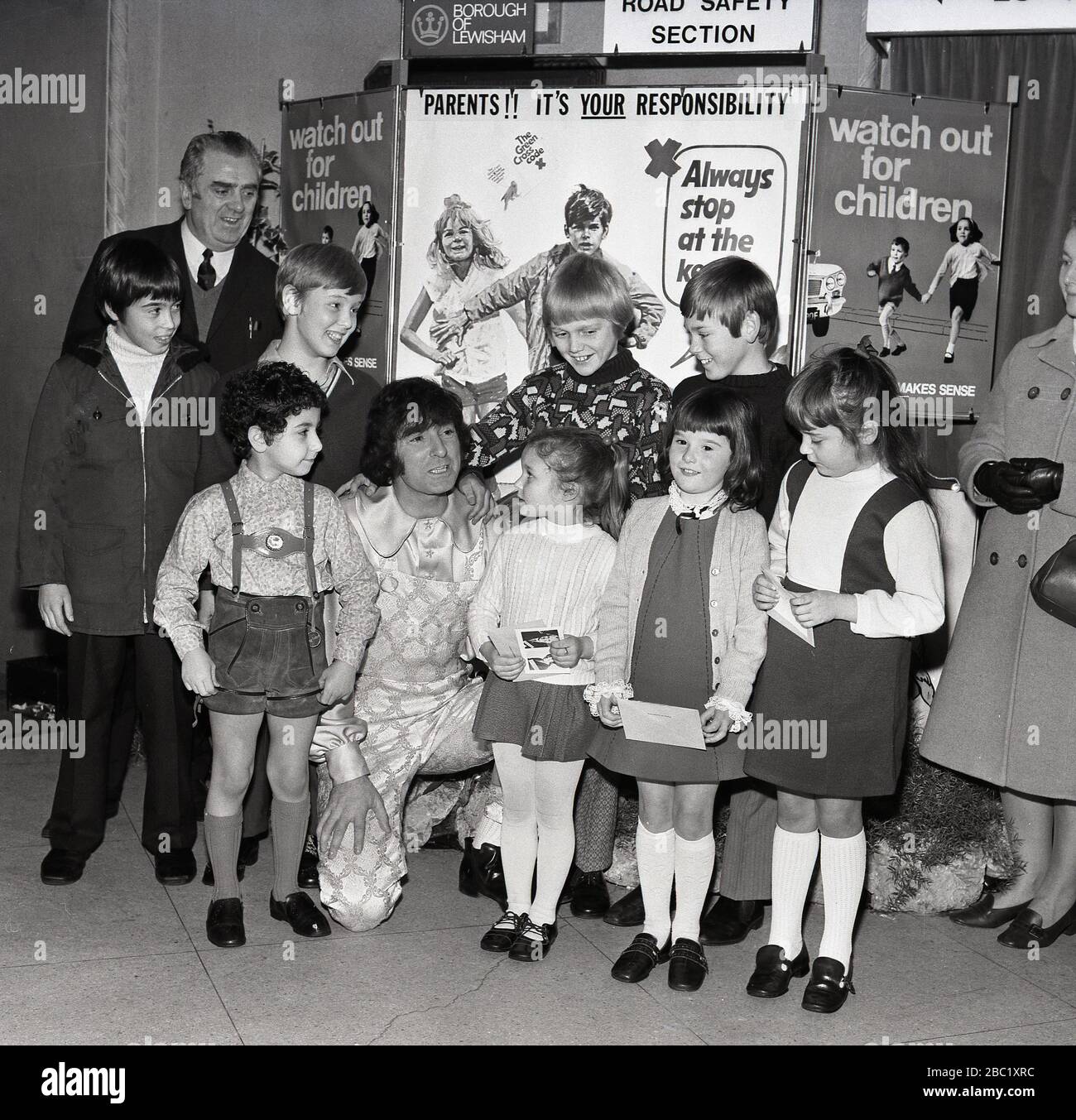 Der britische Comedian und Entertainer der Kinder, Ken Goodwin, mit einer Gruppe von Schulmädchen und Jungen vor Werbeplakaten für die Verkehrssicherheit von Kindern und dem Green Cross Code im Borough of Lewisham, South East London, England, Großbritannien. Stockfoto