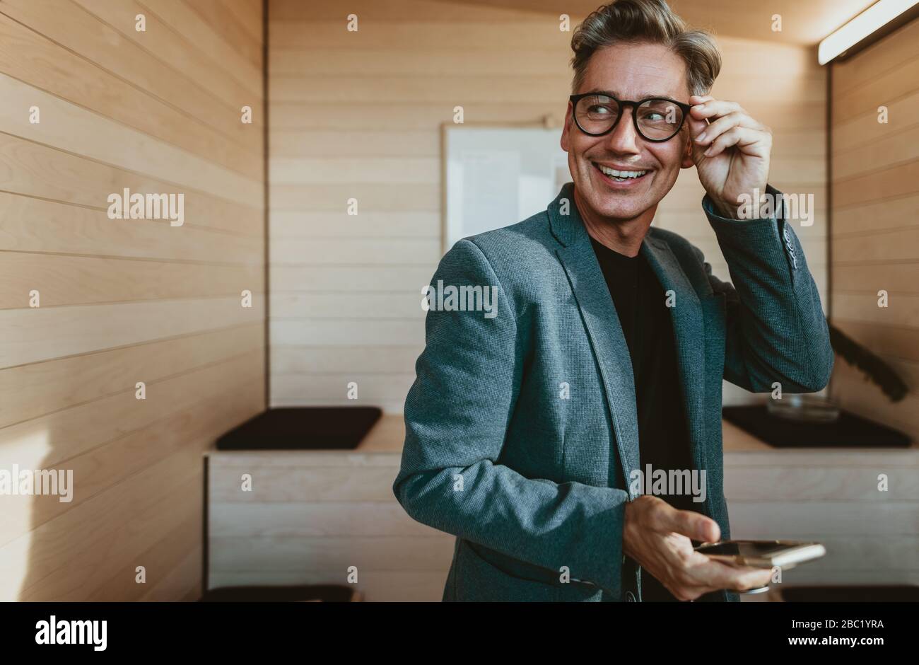 Geschäftsmann im Schulungsraum des Büros, der wegblickt und lächelt. Glücklicher, reifer Geschäftsmann im Büro. Stockfoto