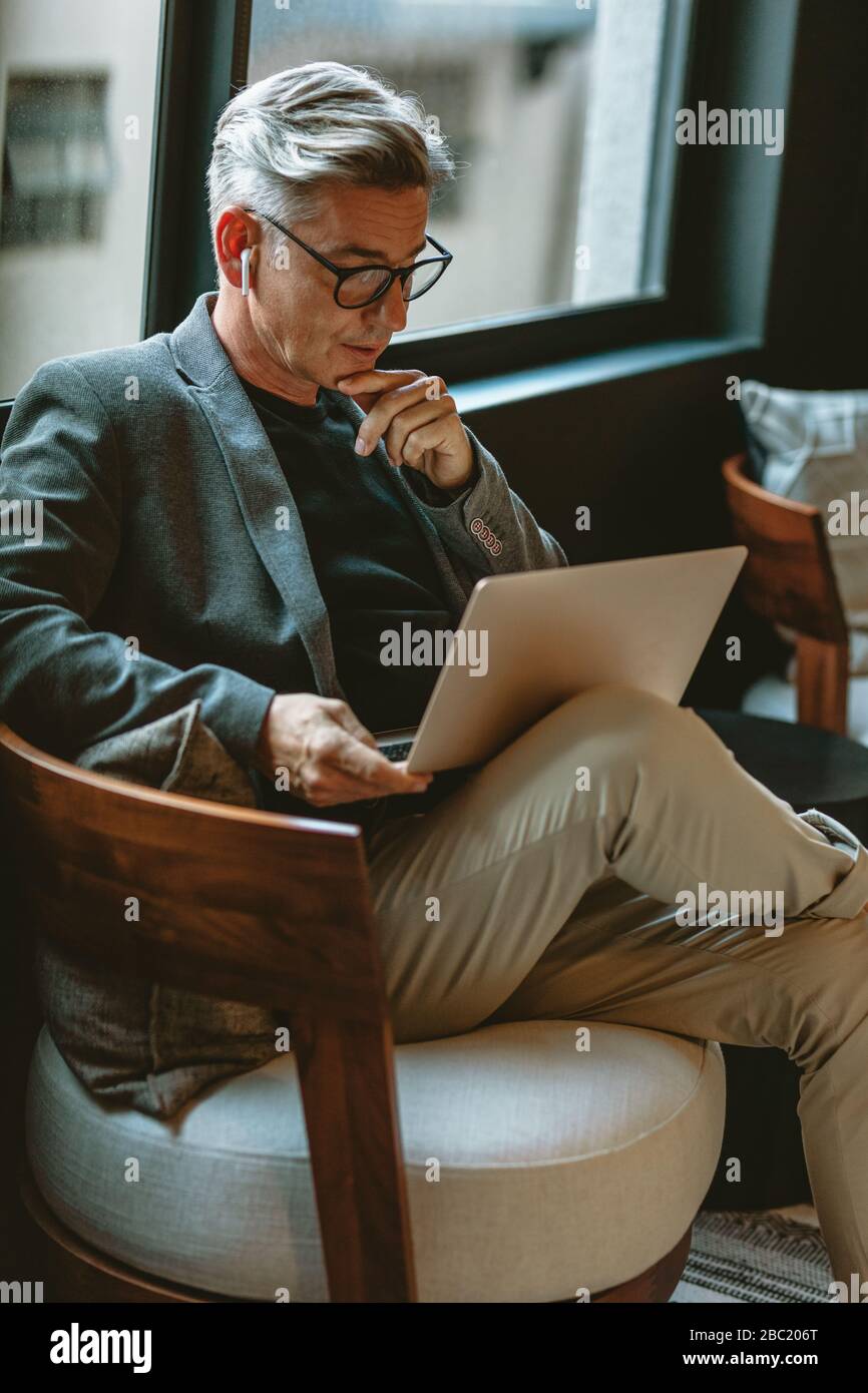 Geschäftsmann, der mit der Arbeit am Laptop beschäftigt ist. Aufmerksamer Geschäftsmann liest E-Mails auf Laptop in der Lobby des Büros. Stockfoto