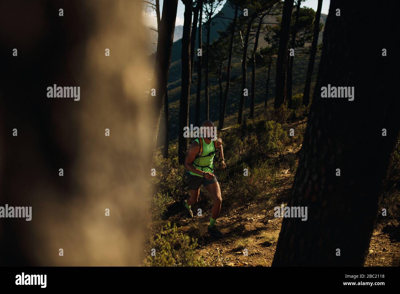 Passen junge Mann in Sportkleidung tragen Hydration Pack läuft im Freien über Rocky Trail auf dem Hügel. Mountain Trail Runner üben auf Schmutz weg. Stockfoto