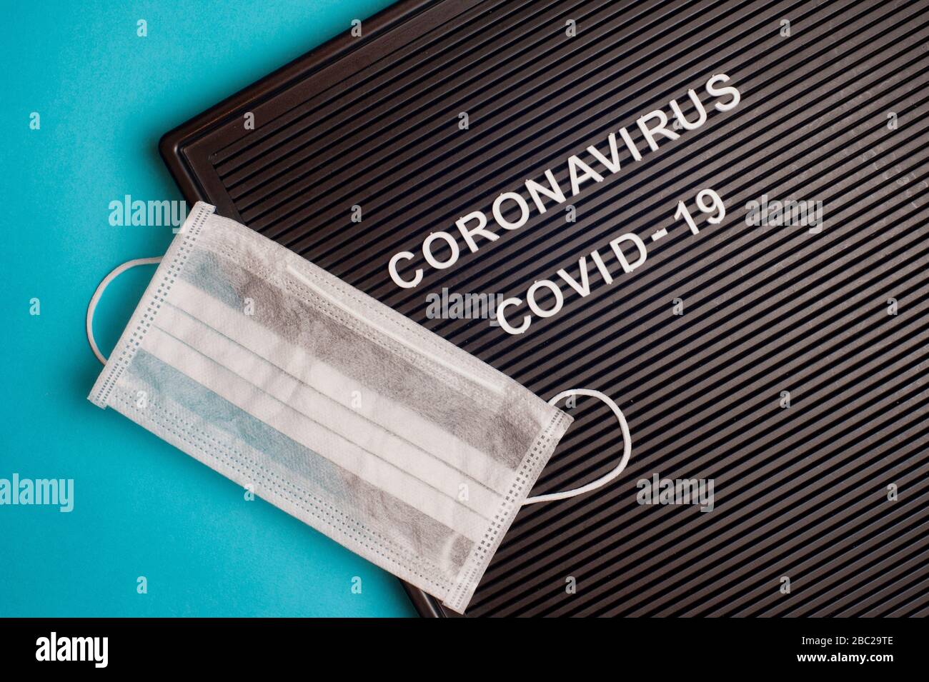 Coronavirus - COVID -19 - Text auf schwarzem Buchstaben und chirurgischer Maske. Stockfoto
