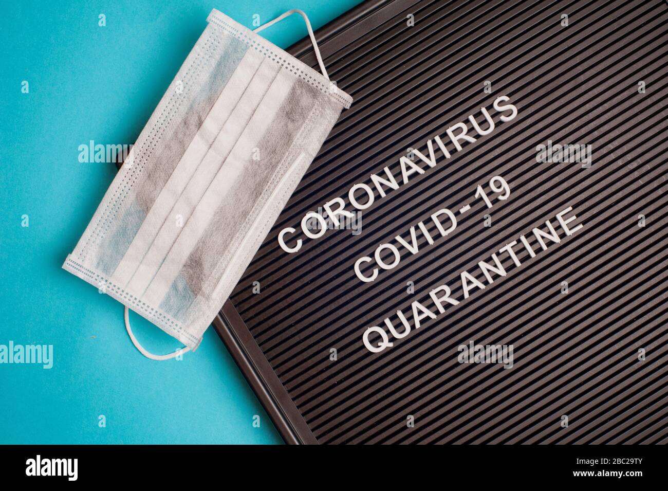 Coronavirus - COVID -19 Quarantäne - Text auf schwarzem Briefbrett und chirurgischer Maske. Stockfoto