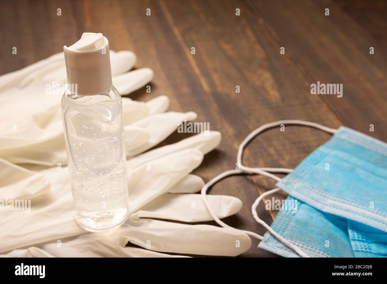 Medizinische Latexhandschuhe, Schutzmasken und Händededesinfektions-Gelflasche zum Schutz vor Holzhintergrund. Nützlich für das Konzept der Pandemieprävention Stockfoto