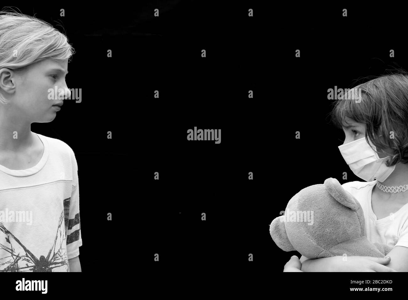 Schwarz-Weiß-Porträt der sozialen Distanz zwischen zwei kleinen Kindern, eines trägt Gesichtsmaske und hält Teddybär Stockfoto