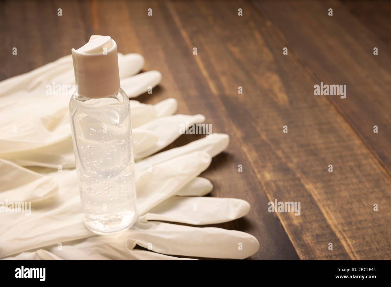 Medizinische Latexhandschuhe und Händededesinfektions-Gelflasche zum Schutz vor Holzhintergrund. Nützlich für das Konzept der Pandemieprävention Stockfoto