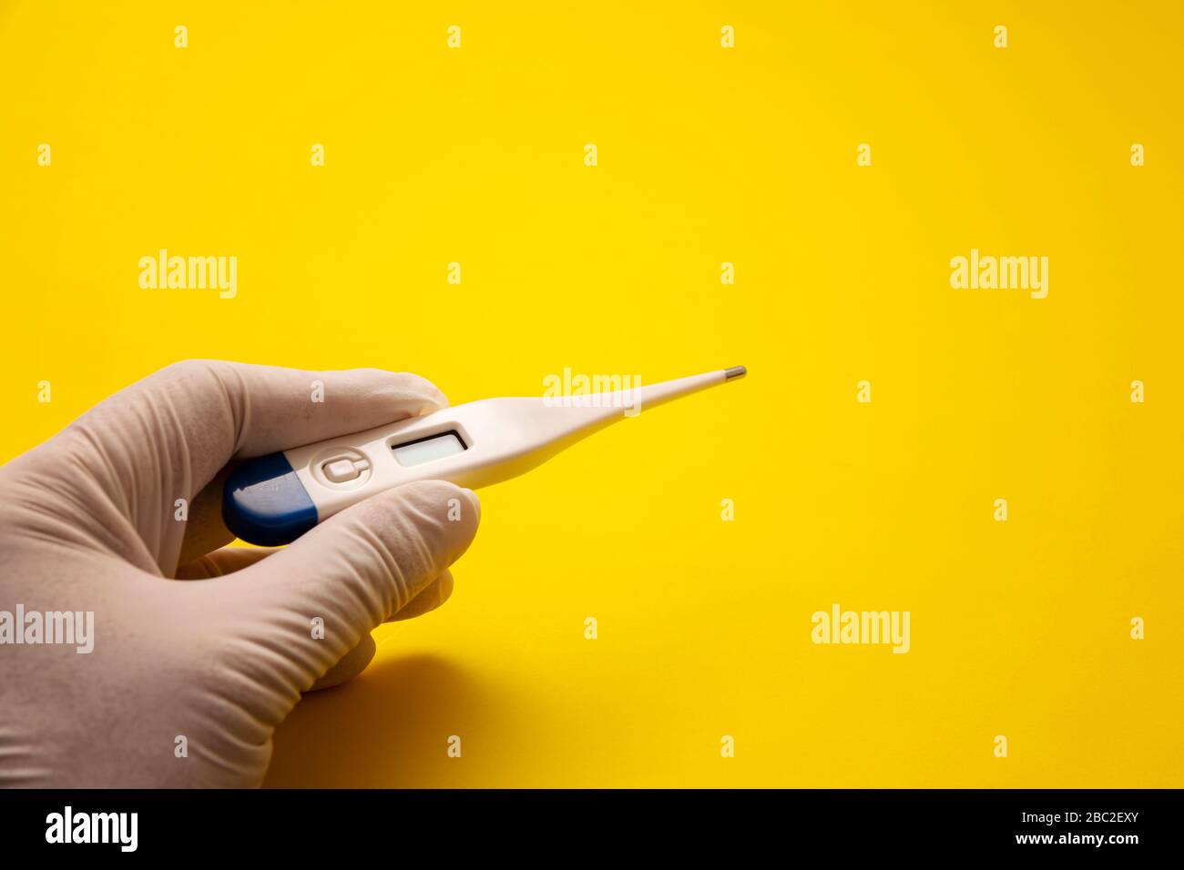 Hand mit medizinischem Latexhandschuh, der ein Digitalthermometer auf gelbem Hintergrund hält. Fieber und Gesundheitskonzept. Kopierbereich Stockfoto Hand mit medizinischem Latexhandschuh, der ein Digitalthermometer auf gelbem Hintergrund hält. Fieber und Gesundheitskonzept. Kopierbereich Stockfoto