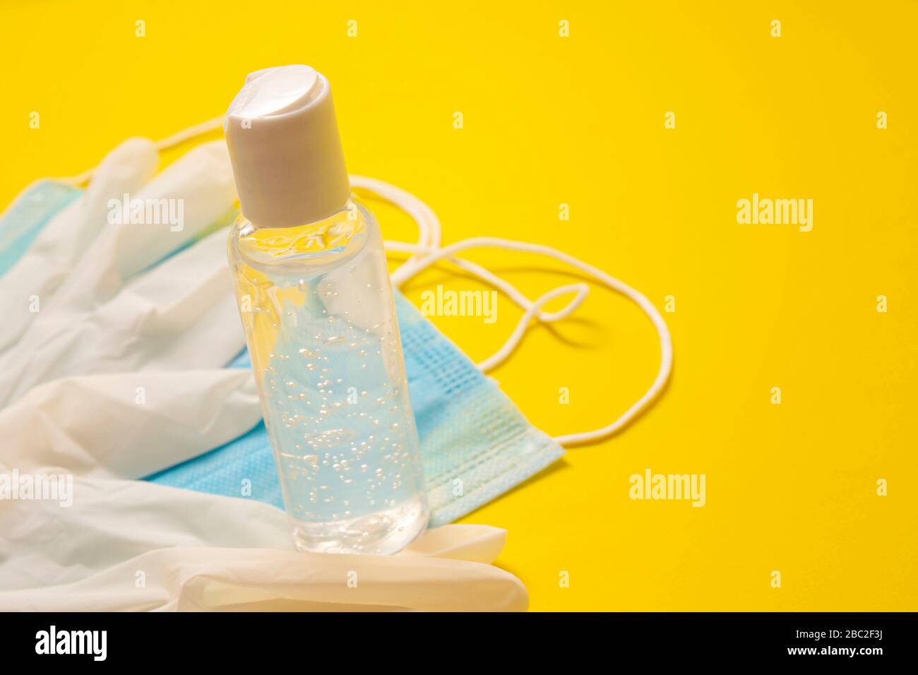 Medizinische Latexhandschuhe, Schutzmasken und Händededesinfektions-Gelflasche zum Schutz vor gelbem Hintergrund. Nützlich für das Konzept der Pandemieprävention Stockfoto