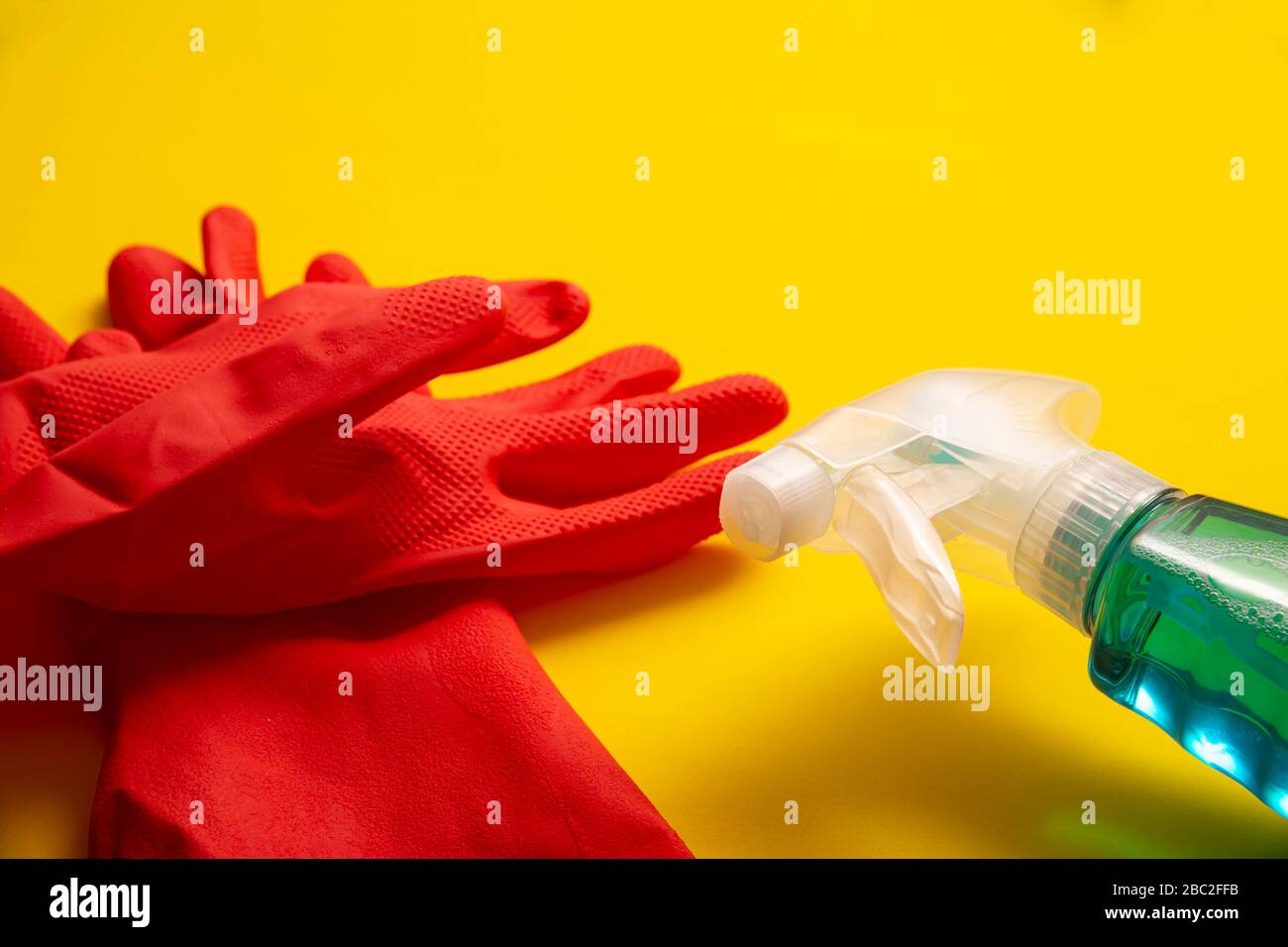 Rote Gummihandschuhe und Flüssigwaschmittel in Sparrenflasche auf gelbem Hintergrund, Reinigungs- und Sanierungskonzept Stockfoto