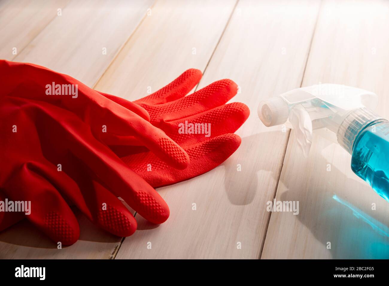 Rote Gummihandschuhe und Flüssigwaschmittel in Sparrierflasche auf Holzhintergrund, Reinigungs- und Sanierungskonzept Stockfoto