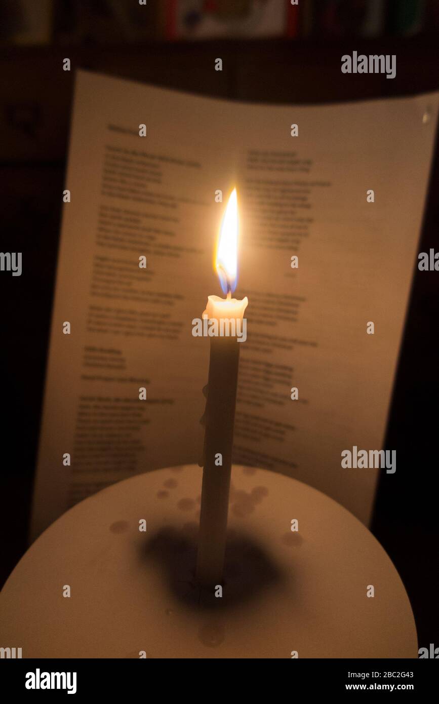 Kirche Kerze mit einer brennenden Flamme fotografiert während eines Weihnachtsliedservice Konzert in Weihnachten. Die Worte der Weihnachtslieder sind auf dem Gesangblatt dahinter zu sehen. England Großbritannien (116) Stockfoto