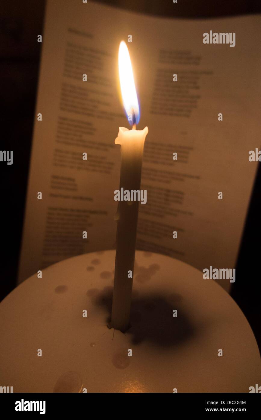 Kirche Kerze mit einer brennenden Flamme fotografiert während eines Weihnachtsliedservice Konzert in Weihnachten. Die Worte der Weihnachtslieder sind auf dem Gesangblatt dahinter zu sehen. England Großbritannien (116) Stockfoto