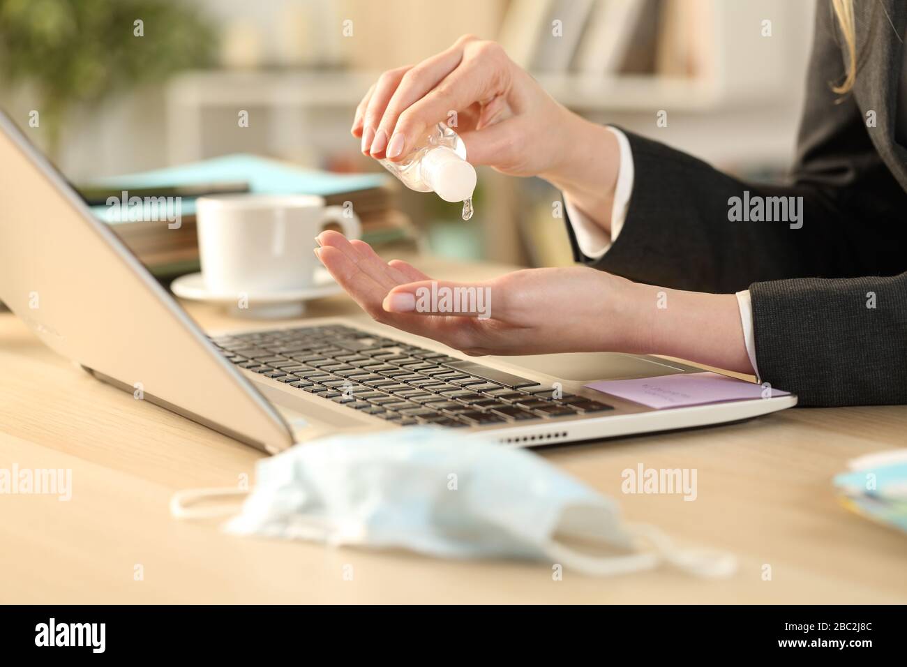 Nahaufnahme der Unternehmerin mit einem Laptop, der die Hände mit Desinfektionsgel desinfiziert, um Ansteckungsgefahr zu vermeiden, die auf einem Schreibtisch im Büro sitzt Stockfoto