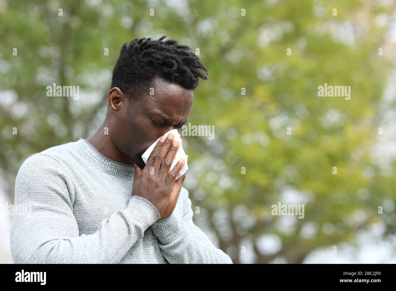 Allergischer schwarzer Mann bläst in einem Park an einem sonnigen Tag in der Frühlingssaison Stockfoto