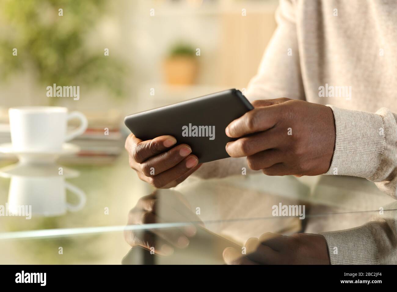 Nahaufnahme von Black man Hands Spielen von Videospielen auf Smartphone Sitzen auf einem Schreibtisch zu Hause Stockfoto