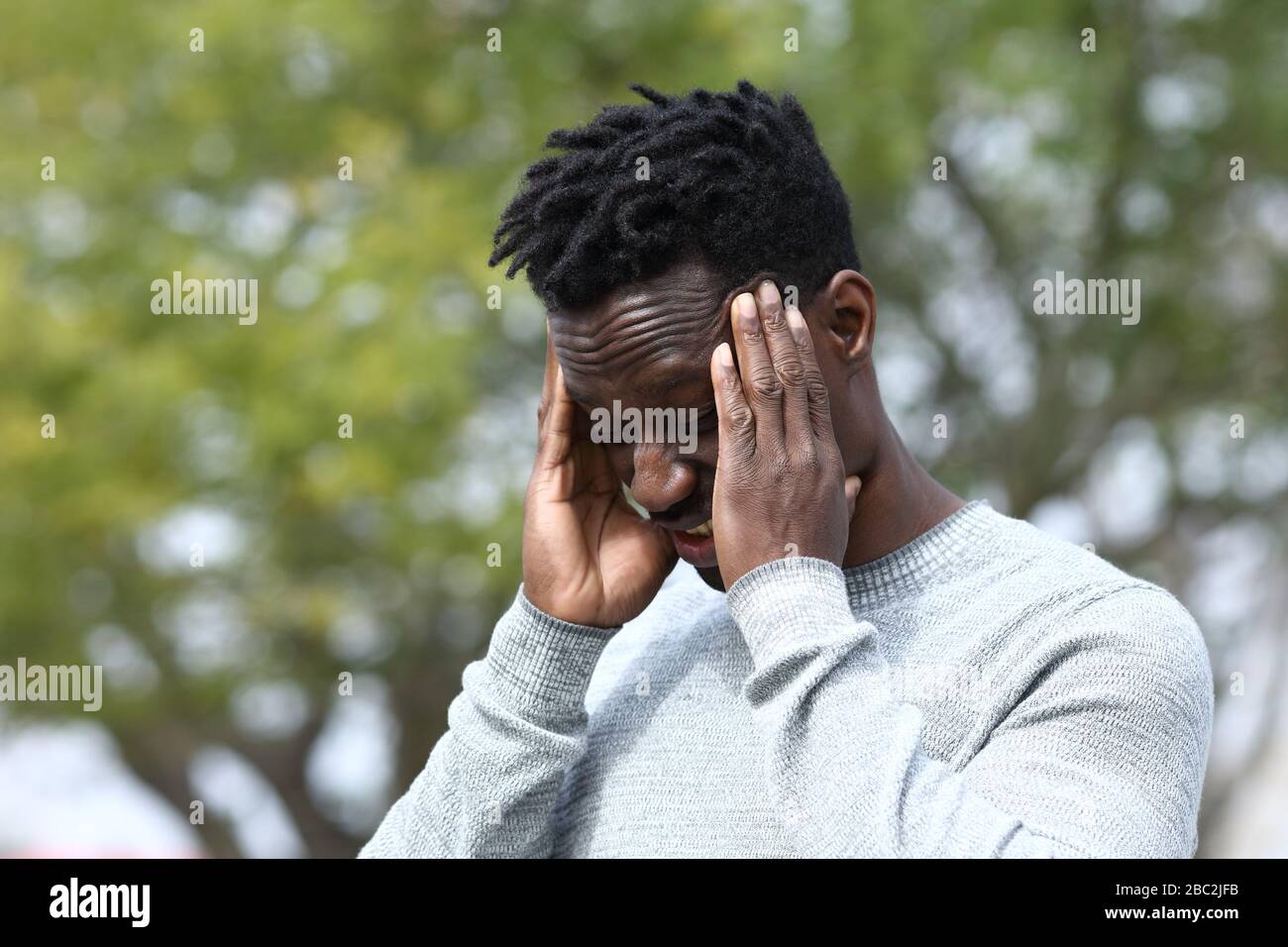 Schwarzer Mann, der an schweren Migräne-Reibtempeln in einem Park leidet Stockfoto