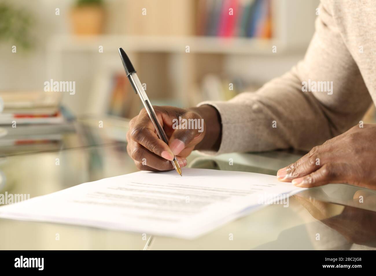 Nahaufnahme der schwarzen Hände, die das Dokument auf einem Schreibtisch zu Hause signieren Stockfoto