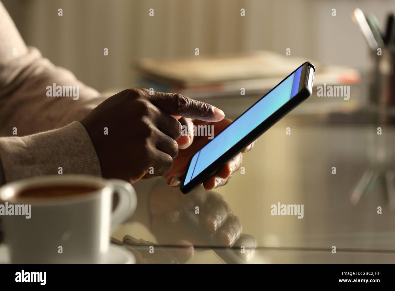 Seitenansicht Nahaufnahme Porträt eines schwarzen Mannes Hände mit Handy auf einem Schreibtisch in der Nacht zu Hause oder im Büro Stockfoto