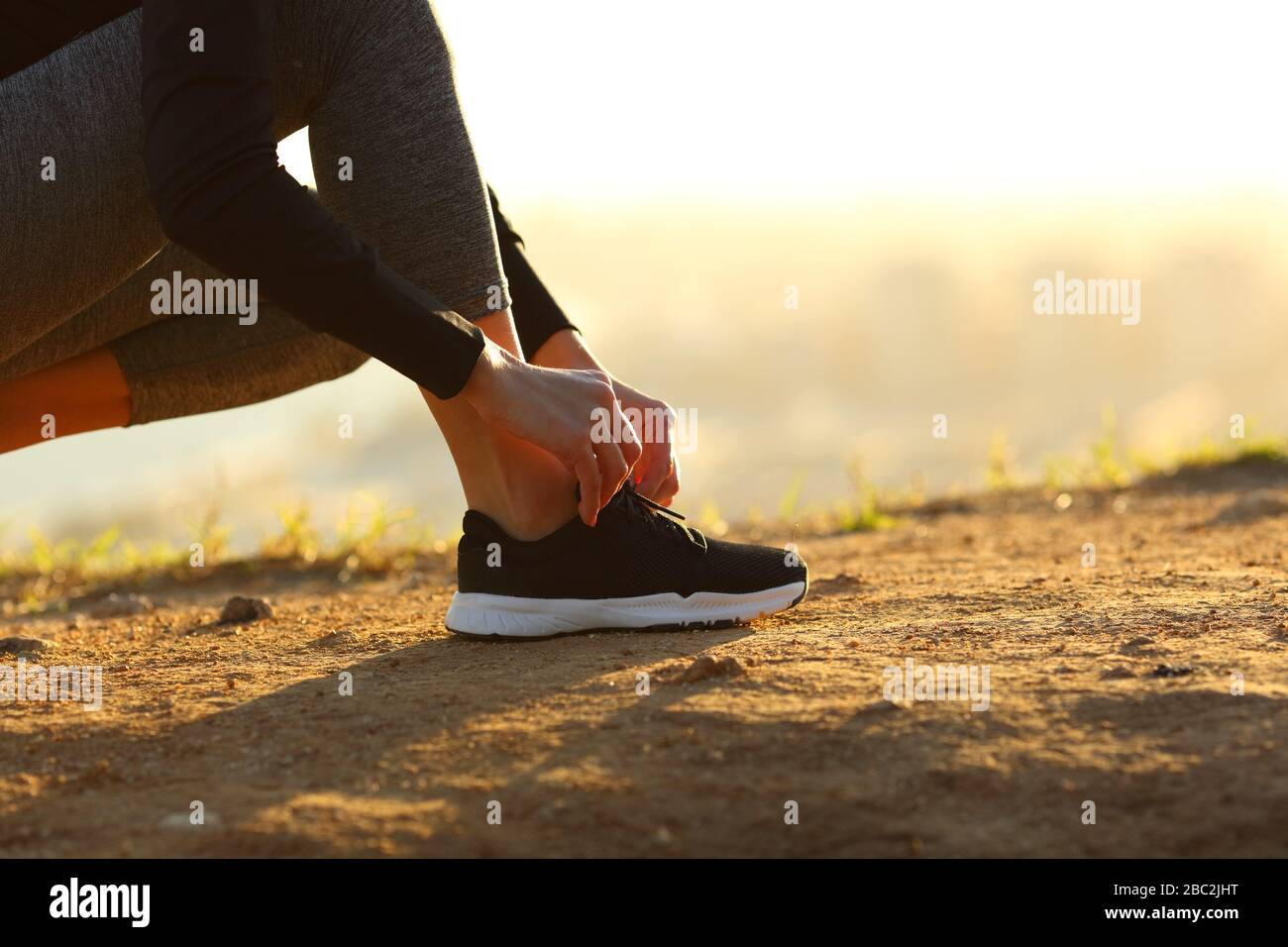 Seitenansicht Nahaufnahme der Hände der Läuferin, die bei Sonnenuntergang Schnürsenkel von Schuhen auf dem Boden bindet Stockfoto