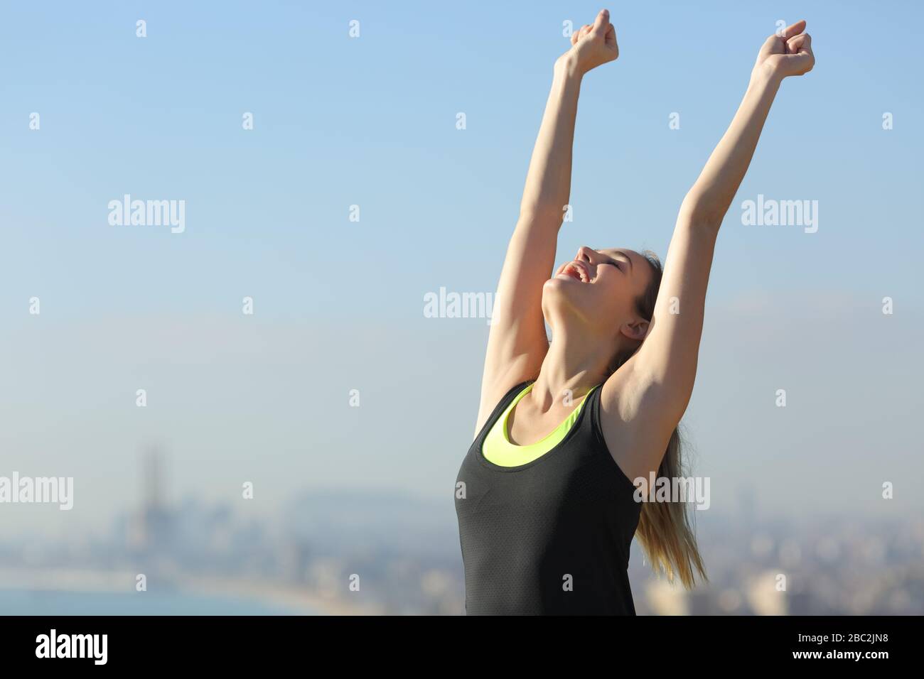 Aufgeregte Läuferin hebt Arme und feiert an einem sonnigen Tag Erfolg in den Außenbezirken der Stadt Stockfoto
