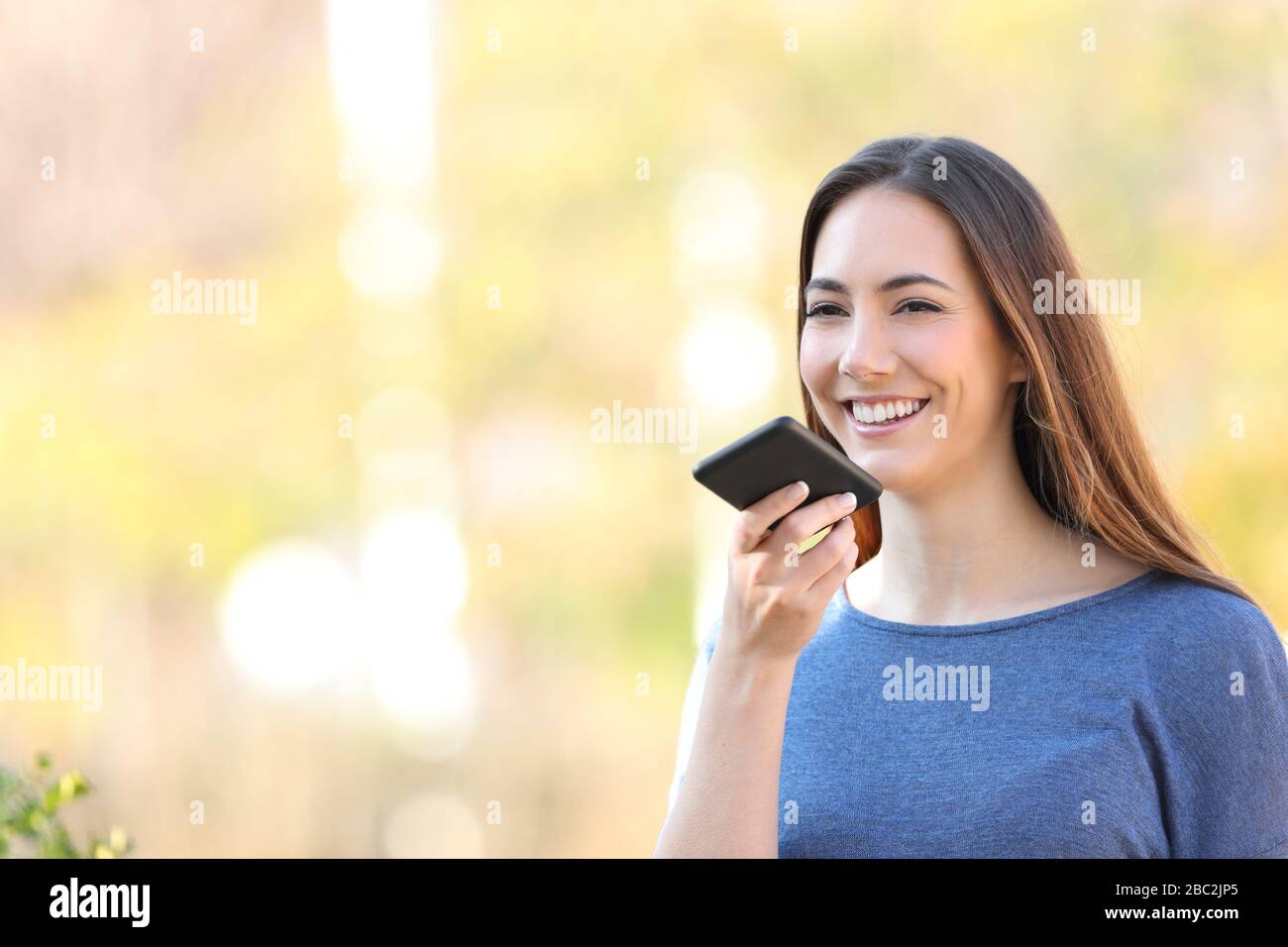 Glückliches Mädchen, das sms mit Spracherkennung auf dem Handy in einem Park aufzeichnet Stockfoto