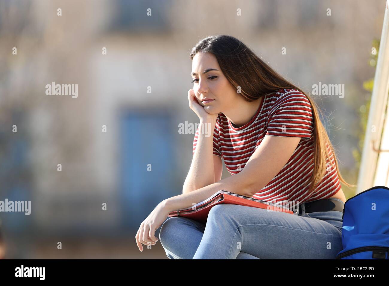 Frustrierte Studentin beschwert sich, in einem Campus sitzend hinunterzuschauen Stockfoto