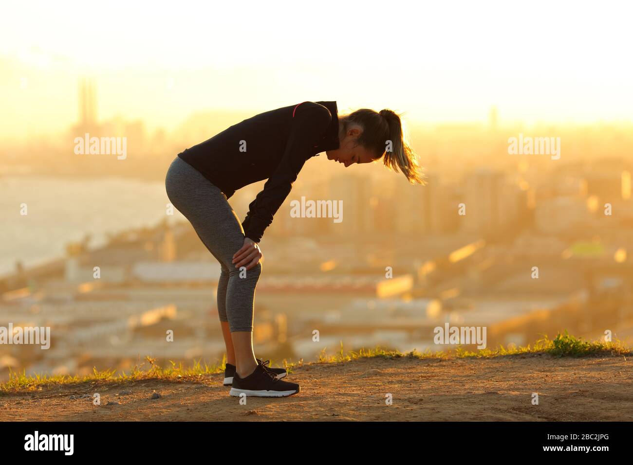 Profil eines erschöpften Läufers, der sich nach dem laufen in den Randgebieten der Stadt bei Sonnenuntergang ausruht Stockfoto