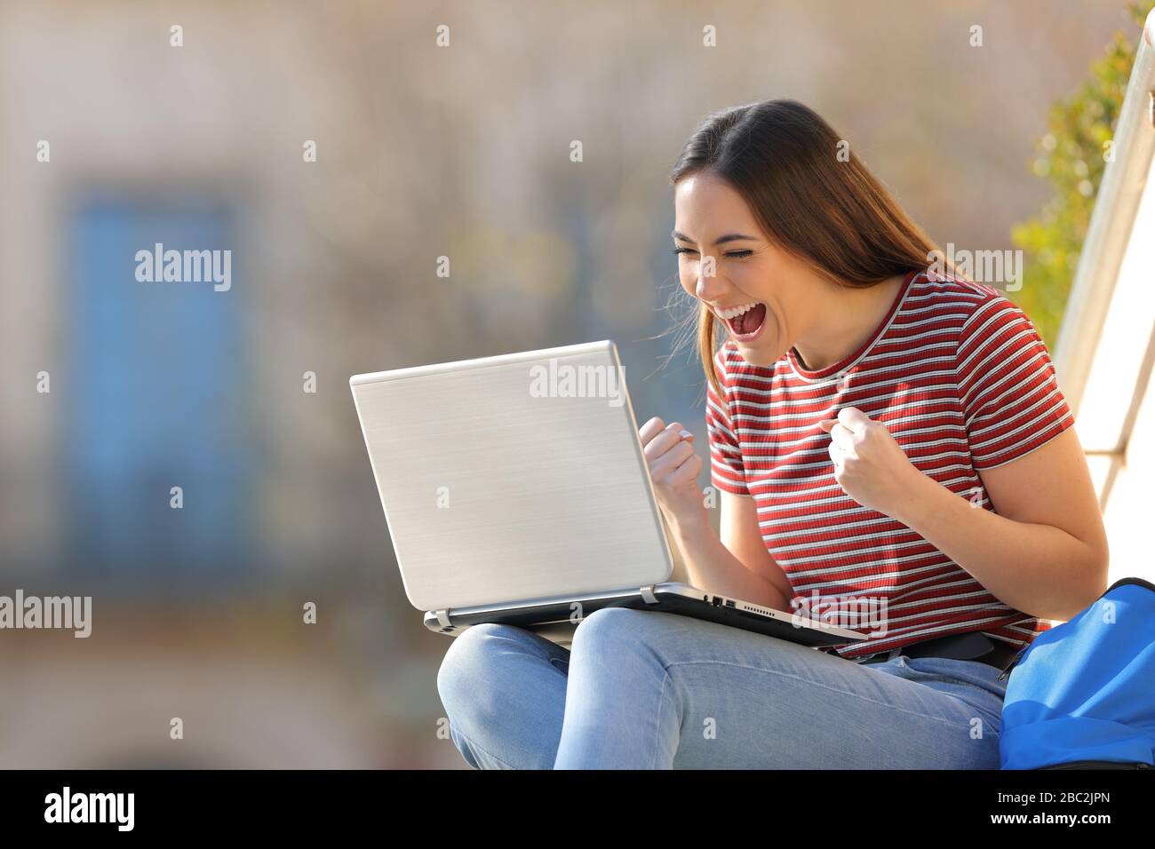 Aufgeregte Studenten, die gute Nachrichten auf einem Laptop im Freien auf einem Universitätsgelände lesen Stockfoto