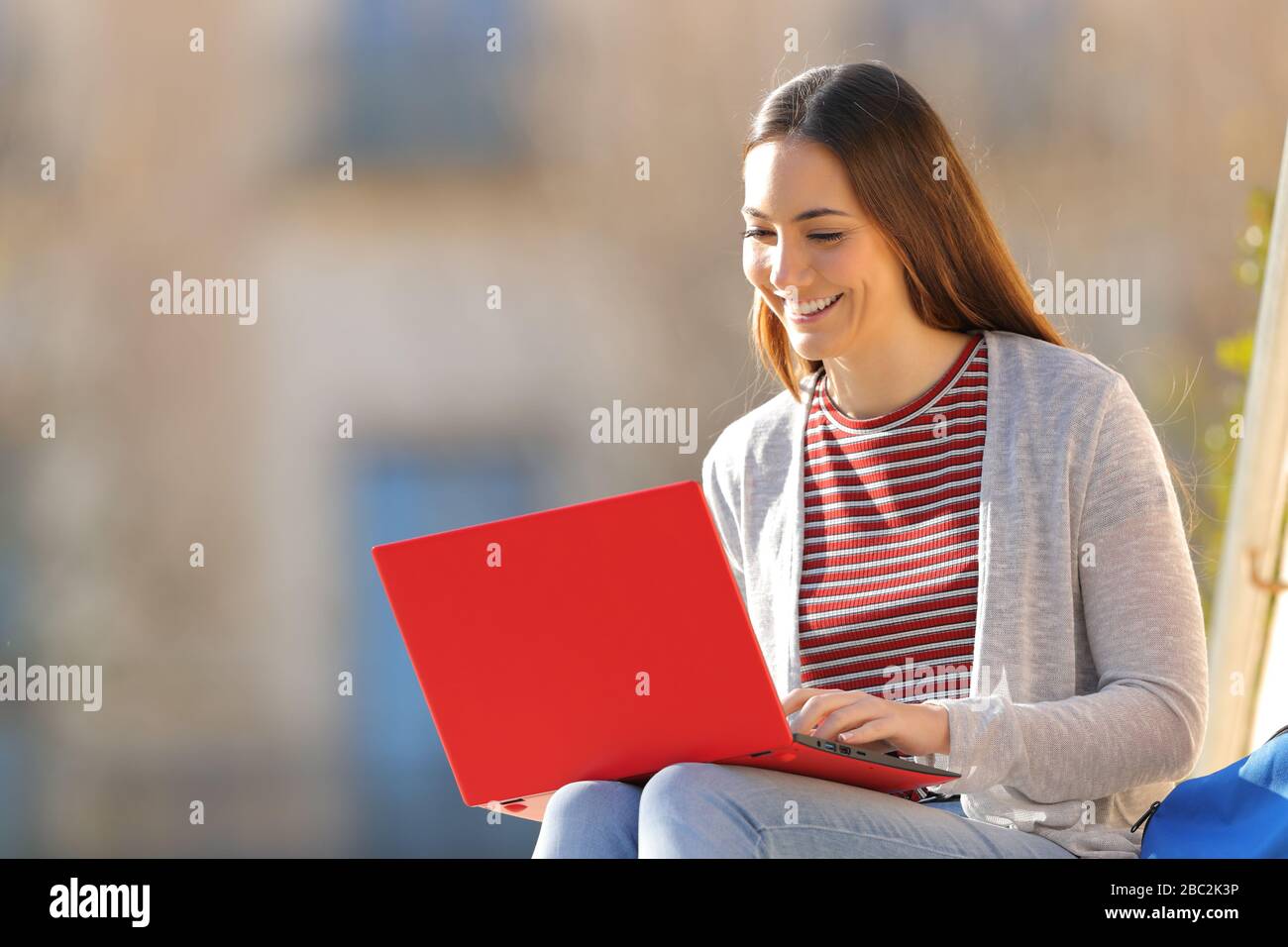 Fröhliches E-learning mit rotem Laptop an einem sonnigen Tag auf einem Campus Stockfoto
