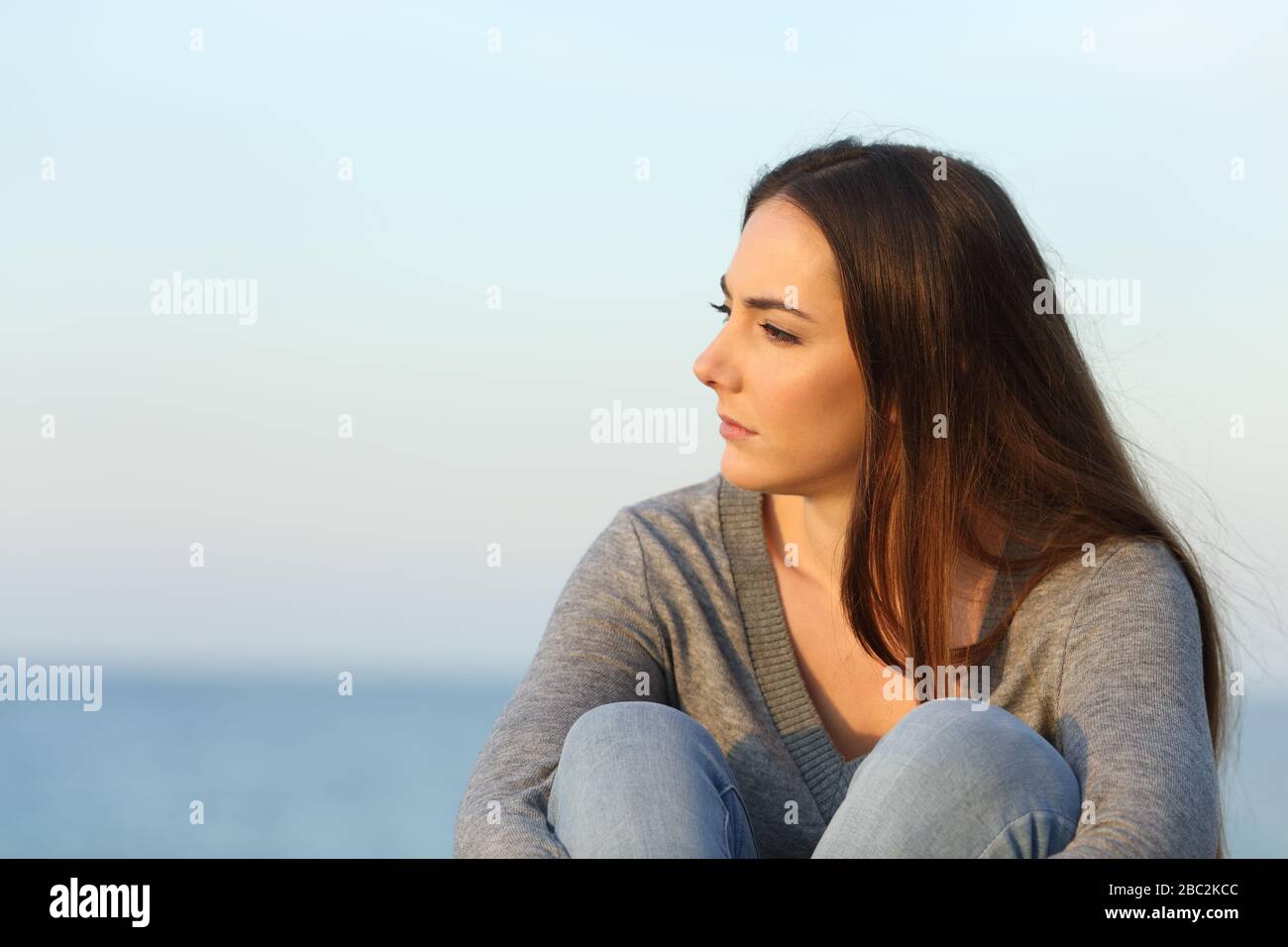 Nachdenkliche melancholische Frau, die bei Sonnenuntergang am Strand sitzt Stockfoto