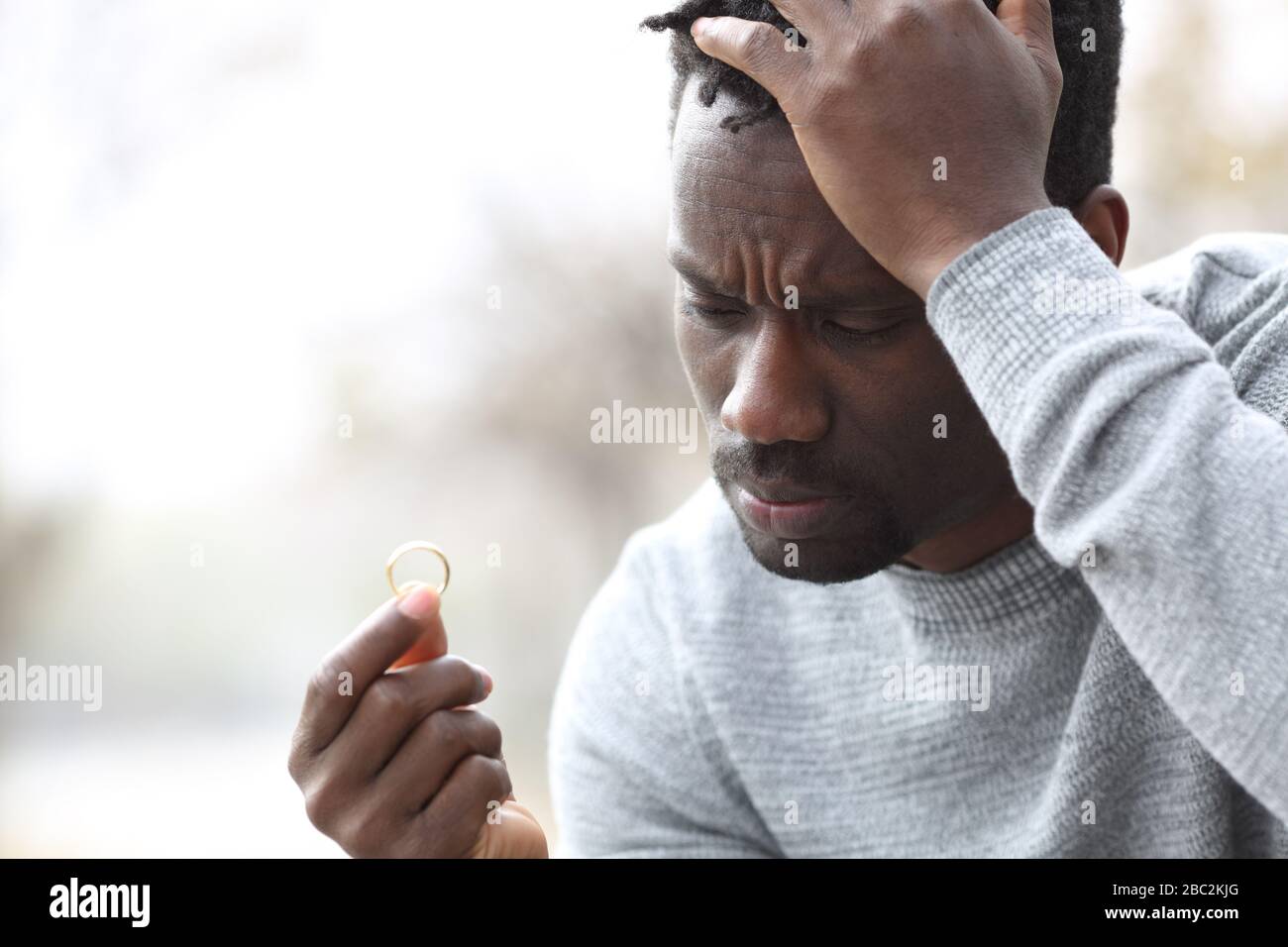Trauriger schwarzer Mann, der sich beschwert, auf den Hochzeitsring im Freien in einem Park zu schauen Stockfoto