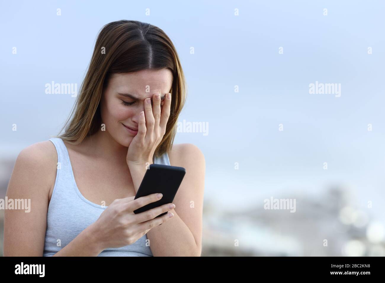 Traurige Frau, die im Freien auf dem Handy schlechte Nachrichten überprüft Stockfoto