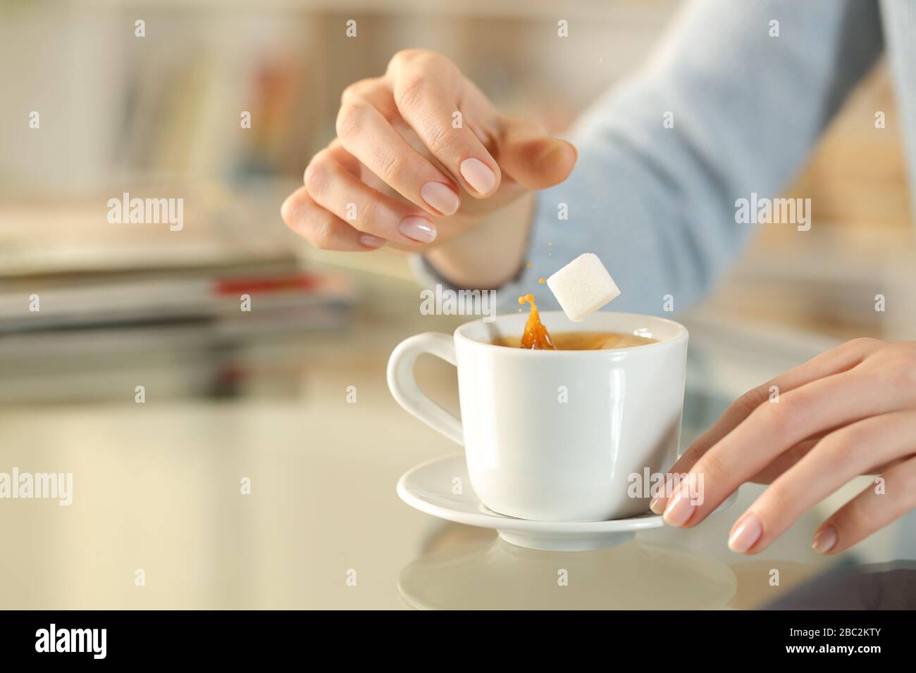 Nahaufnahme der Frau, die zuckersüßen Würfel auf eine Kaffeetasse auf einem Schreibtisch zu Hause wirft Stockfoto