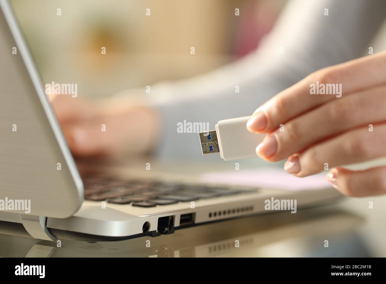 Nahaufnahme der Hände der Frau, die das usb-Flash-Laufwerk neben dem Laptop auf einem Schreibtisch zu Hause halten Stockfoto