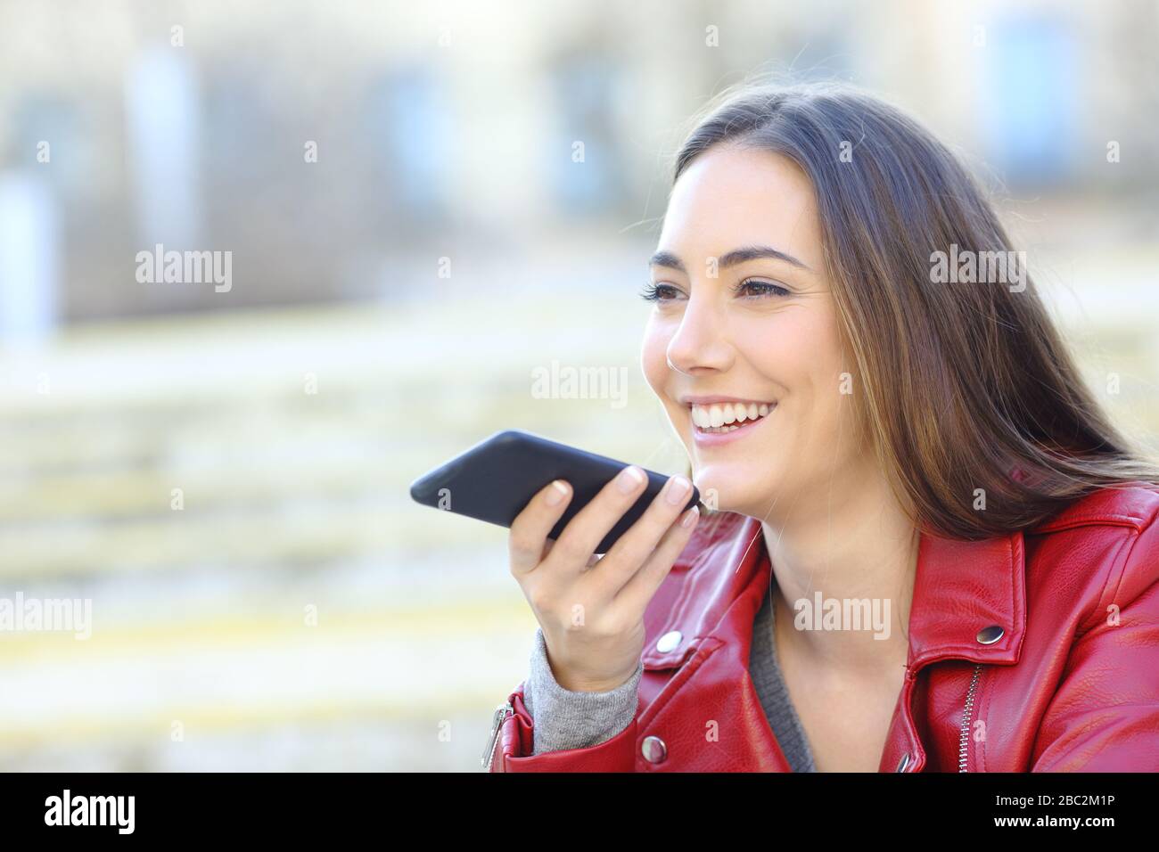 Glückliche Frau in rotem Aufnahmetext mit Spracherkennung auf dem Handy auf der Straße Stockfoto
