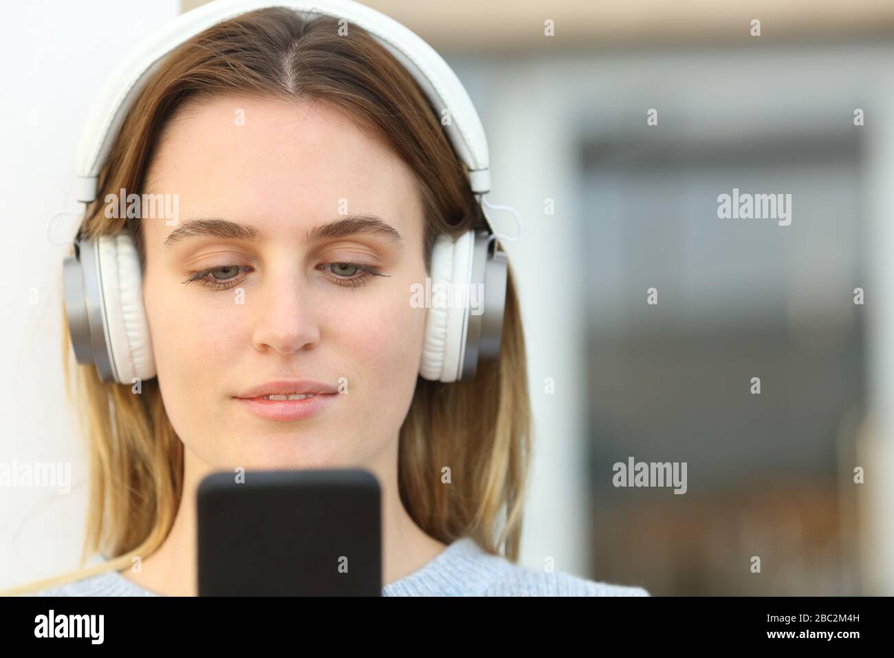 Vorderansicht Portrait einer Frau mit Kopfhörern, die Musik auf einem Smartphone auf einer Terrasse hören Stockfoto
